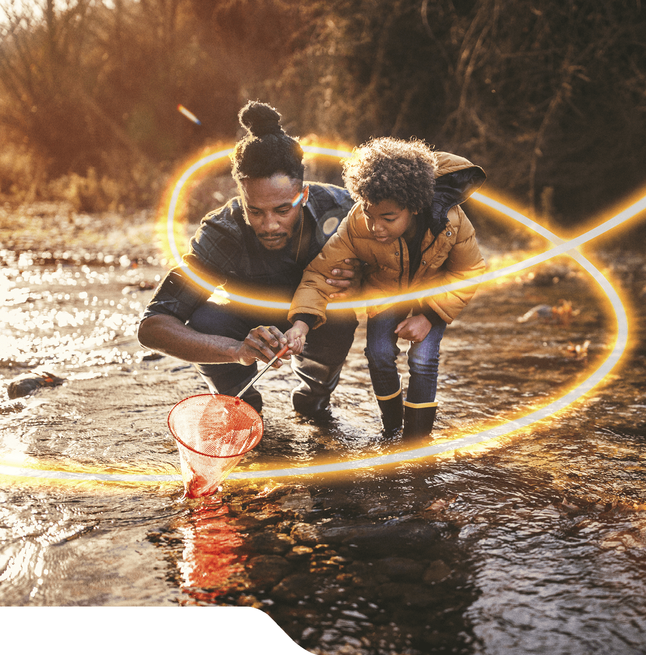 Young dad teaching son how to fish with fishing net in mountain stream at sunset